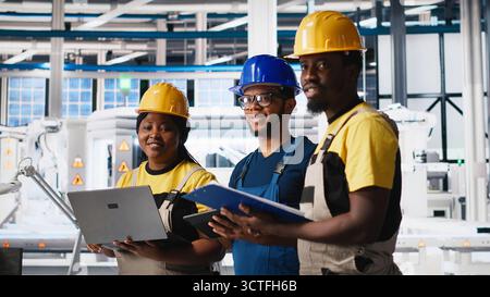 Gruppe schwarzer Mitarbeiter im Werk für Solarpaneele, die Daten auf Geräten und Dokumenten überprüfen. Ingenieure von Photovoltaik-Anlagen, die an innovativen Solarzellen arbeiten, entwickeln einen Prototypen. Kamera A.. Stockfoto