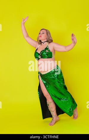 Reife Tänzerin im Tanzoutfit posiert und tritt in voller Länge vor gelbem Hintergrund auf. Sinnlichkeit kaukasische Frau in grüner sequi Stockfoto