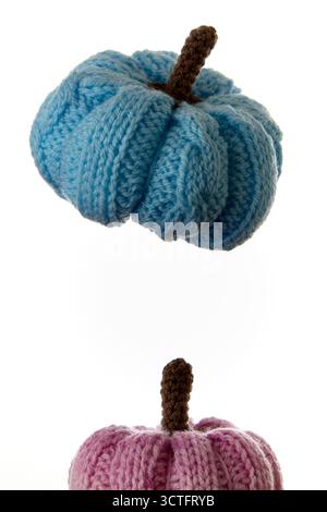 Vertikale Anordnung von blauen und rosa gestrickten Kürbissen, fotografiert auf weißem Hintergrund im minimalistischen Stil. Ideal für gemütliche Herbstdekoration, Heimwerkerarbeit oder Textil Stockfoto
