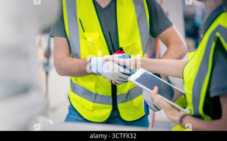 Ingenieurmechaniker schütteln Hand in der Stahlwerkstatt. Programmiersoftware für Industrieroboter für automatisierte Fertigungstechnologie Stockfoto