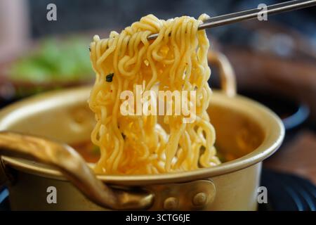 Scharfe koreanische Instant-Ramen-Nudeln in einem traditionellen Topf, mit Essstäbchen gehoben. Stockfoto