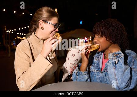 Verschiedene junge Frauen teilen sich Churros auf dem Nachtmarkt Stockfoto