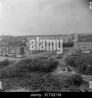 Die massive städtische Expansion in den 1970er Jahren Sloviansk, ukrainische SSR, wird in diesem Panoramablick auf das im Bau befindliche Artema-Mikroviertel erfasst. Ein riesiger, neunstöckiger Wohnblock mit „Breschnevka“-Paneelwand dominiert die Szene, ein Markenzeichen der Massenbauprojekte dieser Epoche. Im Vordergrund arbeitet ein Turmkran auf dem Fundament eines anderen Gebäudes, der den industrialisierten Bauprozess in Aktion zeigt. Der neue Stadtteil erhebt sich direkt am Stadtrand, grenzt an Wälder und Felder und symbolisiert den ehrgeizigen Versuch, moderne Häuser zu schaffen Stockfoto