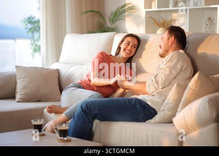 Glückliches verliebtes Paar, das Hände hält und sich zuhause auf einer Couch ansieht Stockfoto