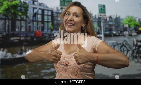 Eine hispanische Frau mittleren Alters gibt auf der Straße eine Geste mit doppeltem Daumen hoch; Selbstvertrauen ermutigt Optimismus. Stockfoto