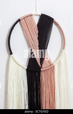 Dekorativer Wandaufhänger aus Garn mit weißem und schwarzem Design. Das Garn ist so angeordnet, dass ein Gefühl von Bewegung und Fließfähigkeit entsteht. Die Farbe Stockfoto