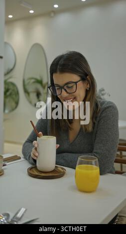 Frau genießt Kaffee drinnen in einem modernen Luxusrestaurant mit heller Beleuchtung, stilvoller Einrichtung und entspannter Atmosphäre und schlürft ruhig ein Getränk Stockfoto