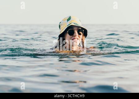 Frau Sonnenbrille Meer - Eine junge Frau mit Sonnenbrille schwimmt an einem sonnigen Tag im Meer. Stockfoto