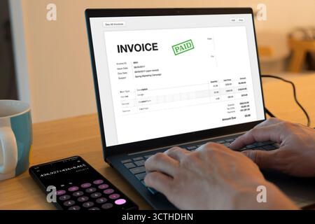 Digitale Rechnung mit bezahltem Stempel auf dem Laptop-Bildschirm, Smartphone-Rechner neben Kaffeetasse. Konzept für Online-Abrechnung, Finanzmanagement, A Stockfoto
