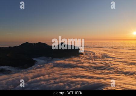 Sonnenaufgang glüht über Berggipfeln und einem Wolkenmeer, Schweiz Stockfoto