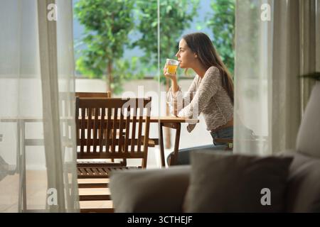 Profil einer Teetrinkenden Frau, die auf einer Terrasse in einem Haus sitzt Stockfoto