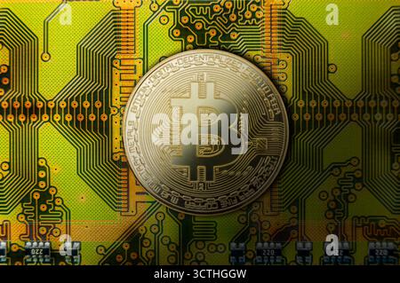 Die Goldmünze, die digitale Währung symbolisiert, liegt auf einer komplexen grünen Leiterplatte, die die Verbindung zur Blockchain-Technologie unterstreicht. Stockfoto