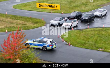 07. Oktober 2025, Niedersachsen, Laatzen: Ein mit Car2X ausgerüstetes Fahrzeug der Autobahnpolizei Hannover passiert während einer Demonstration wartende Fahrzeuge auf dem Gelände des ADAC-Fahrsicherheitszentrums (Luftbild mit Drohne). Alle Fahrzeuge auf der Demonstration kommunizieren über Car2X-Kommunikation miteinander, die häufig bereits bei Herstellern wie Volkswagen und Volvo serienmäßig eingebaut wird. Dank ihrer vielen Sensoren erkennen die Autos Gefahren oder können sich auch als Rettungsfahrzeuge auf einem Alarmantrieb bekannt machen – und warnen automatisch andere Verkehrsteilnehmer in der Nähe. Ein Sympo Stockfoto