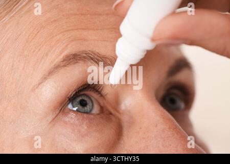Frau, die Augentropfen auf hellem Hintergrund aufträgt, Nahaufnahme Stockfoto