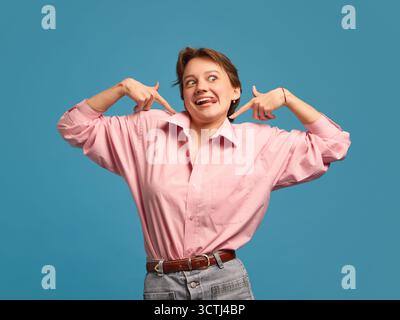 Verspielte Frau, die mit komischem, lustigem Gesichtsausdruck auf sich zeigt Stockfoto