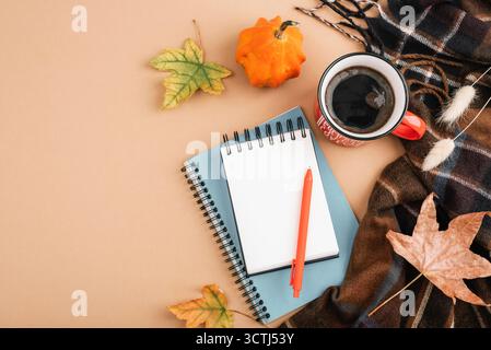 Herbst flach liegend mit Kaffeetasse, Notizbüchern, Stift, Kürbis, Blättern und kariertem Schal auf beigem Hintergrund. Gemütliches, saisonales Arbeitsraumkonzept. Draufsicht, Mocku Stockfoto