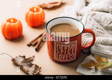 Kaffee-Kürbis-Latte in Orangenbecher, Kerzen und Strickpullover. Stillleben im Herbst, Halloween oder Thanksgiving-Konzept. Nahaufnahme. Stockfoto