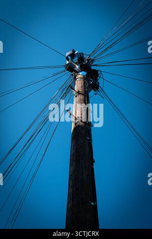 Telegrafenmast mit vielen strahlenden Drähten gegen einen klaren blauen Himmel Stockfoto
