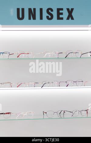 Reihen trendiger Unisex-Brillen sind in einem eleganten Regal in einem optischen Salon ordentlich angeordnet und laden zum Erkunden ein. Stockfoto
