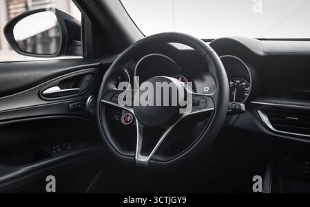 Moderner Innenraum mit Metallakzenten. Lenkrad und Armaturenbrett eines neuen Fahrzeugs, das auf einer Straße geparkt ist. Stockfoto