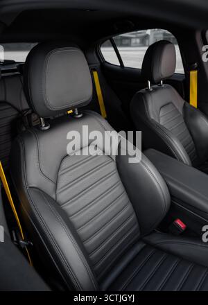 Fahrzeuginnenraum mit sportlichen Sitzen und gelben Sicherheitsgurten. Vordersitz aus Leder eines Kompaktwagens im Fokus und Rückbank im Hintergrund. Moderner Innenraum Stockfoto