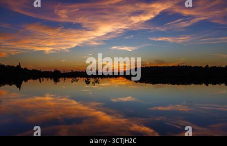 Farbenfroher Sonnenuntergang über stillen Wasser in Pine Barrens, New Jersey, USA. Lebhafte Wolken und Reflexionen erzeugen eine spiegelähnliche, ruhige Szene. Stockfoto
