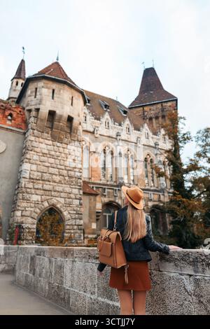 Junge Frau mit Rucksack, die in der Nähe der mittelalterlichen Architektur spaziert, Herbstreise. Stockfoto