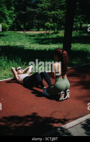 Frauen, die während des Fitnesstrainings im Freien Sit-UPS im Park durchführen Stockfoto