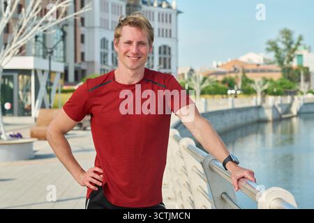 Porträt eines jungen Mannes, der draußen in der Nähe des Urban Riverfront lächelt Stockfoto