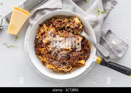 Hausgemachtes Rindfleischragu auf Pasta mit geriebenem Parmesan, fotografiert bei weichem Tageslicht auf strukturiertem weißem Hintergrund für italienische Komfortgerichte. Stockfoto