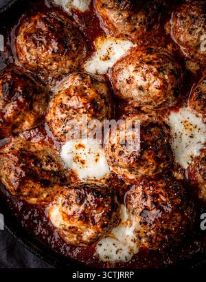 Gebackene Fleischbällchen in Tomatensauce mit geschmolzenem Käse in einer gusseisernen Pfanne, gefangen in stimmungsvollem Tageslicht für ein rustikales Küchendesign. Stockfoto