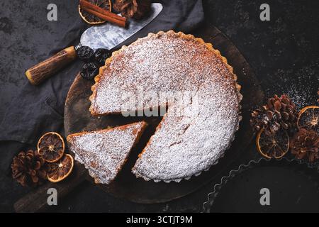 Blick von oben auf eine große Hackkuchen-Torte, die mit Puderzucker mit Tannenzapfen, getrockneten Zitrusfrüchten und Zimt für eine Weihnachtsszene bestäubt ist. Stockfoto