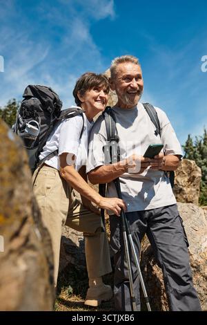 Ein älteres Paar lächelt herzlich, während es die Natur auf einem sonnigen Wanderabenteuer erkundet. Stockfoto