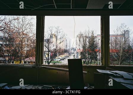 Ein Blick durch das Fenster eines Büros auf eine benachbarte Fabrik. Die Fenster wurden entfernt. Analog aufgenommen, an einem bewölkten Tag. Stockfoto