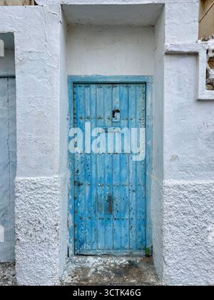 Verwitterte blaue Holztür in einer weißen Stuckwand in Martil, Marokko. Oktober 2025. Stockfoto