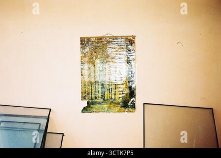 Eine gelbe Mauer in einer verlassenen Fabrik trägt ein großes, altes Poster eines Herbstwaldes mit Fensterscheiben aus entfernten Rahmen, die darunter liegen. Aufnahme ana Stockfoto