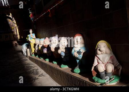 Modellgnome von Schneewittchen und den Sieben Zwergen werden am 4. Oktober 2025 in Neapel, Italien, von einem Schacht von Nachmittagssonne auf einem schmalen Innenhof in der Stadt Ercolano zwischen Neapel und Sorrent beleuchtet. Der Disney-Klassiker aus dem Jahr 1937 entstand 1937, eine Adaption des Märchens Sneewittchen aus dem 19. Jahrhundert, von den Brüdern Grimm. Stockfoto