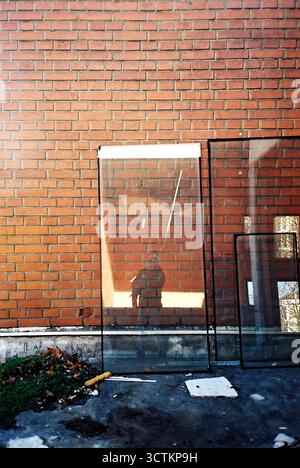 Glas aus einem entfernten Fenster, das sich an eine rote Ziegelwand lehnt und den Fotografen reflektiert. Analoger Film. Stockfoto