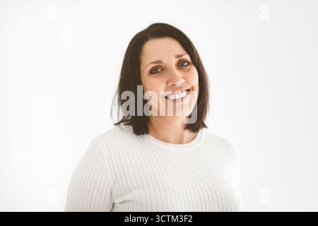 Echte und authentische reife Frau, die in die Kamera blickt und lächelt, während sie vor weißem Hintergrund steht Stockfoto