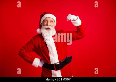 Fröhlicher Weihnachtsmann, der seinen Arm in festlicher Pose auf einem hellen roten Hintergrund beugt, um den Weihnachtsgeist zu feiern Stockfoto