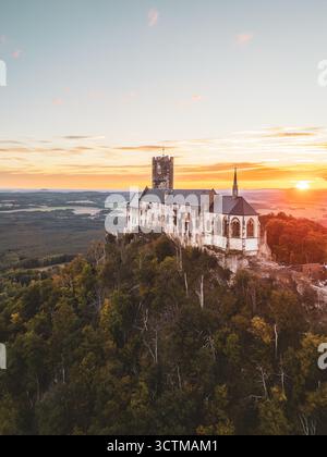 Bezdez Castle steht stolz auf einem Hügel, seine mittelalterlichen Türme bilden sich vor den lebhaften Farben eines Sonnenuntergangs im Sommer in Tschechien. Die alte Ruine strahlt Geschichte aus, während sie von üppigem Grün umgeben ist. Stockfoto
