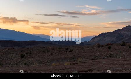Sonnenuntergang im Death Valley mit glühendem goldenem Himmel über mehrschichtigen Bergkämmen, die sanft von warmem Abendlicht beleuchtet werden. Stockfoto