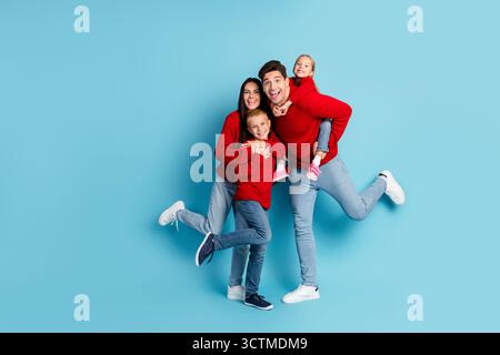 Glückliche Familie in festlichen Pullover, die fröhlich vor blauem Hintergrund hüpfen und gemeinsam Weihnachten feiern Stockfoto