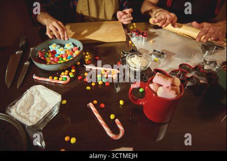 Ein warmer, festlicher Moment in der Küche, wo Familie und Freunde Kekse backen, Süßigkeiten mischen und Leckereien mit Mehl, Nudelnadeln und bunten Bonbons dekorieren Stockfoto