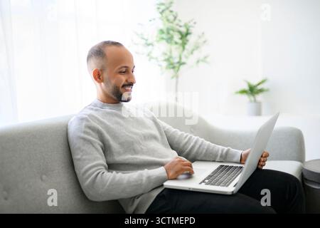 Junger islamischer arabischer Mann, der zu Hause einen Laptop auf dem Sofa benutzt Stockfoto
