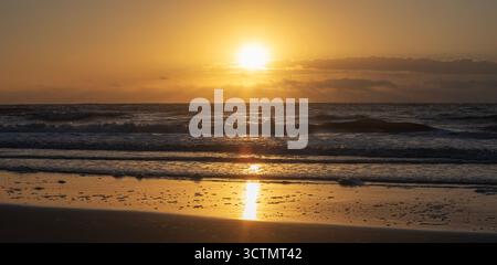 Leuchtend orangefarbene Sonne, die über den Wellen auf der Pawleys Island in South Carolina auf die Atlantikküste aufgeht. Stockfoto