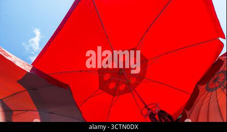 Leuchtend rote Sonnenschirme bieten Schatten vor einem leuchtend blauen, sonnigen Himmel und schaffen ein abstraktes grafisches Muster, das einen entspannten Sommerurlaub symbolisiert Stockfoto