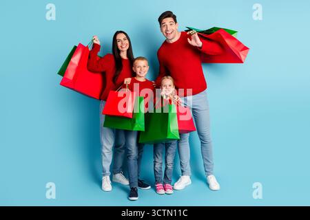 Glückliche Familieneinkäufe während der Weihnachtszeit, posiert mit bunten Einkaufstaschen vor blauem Hintergrund Stockfoto