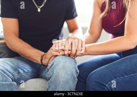 Hand in Hand durch alles. Aufnahme eines unverkennbaren Paares, das die Hände hält, während es zu Hause auf einem Sofa sitzt. Stockfoto