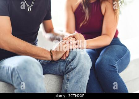 Hand in Hand durch alles. Aufnahme eines unverkennbaren Paares, das die Hände hält, während es zu Hause auf einem Sofa sitzt. Stockfoto